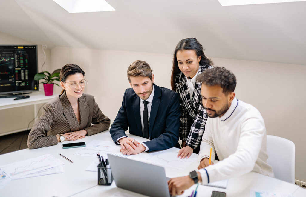 An IT professional shows three coworkers something on a laptop computer.